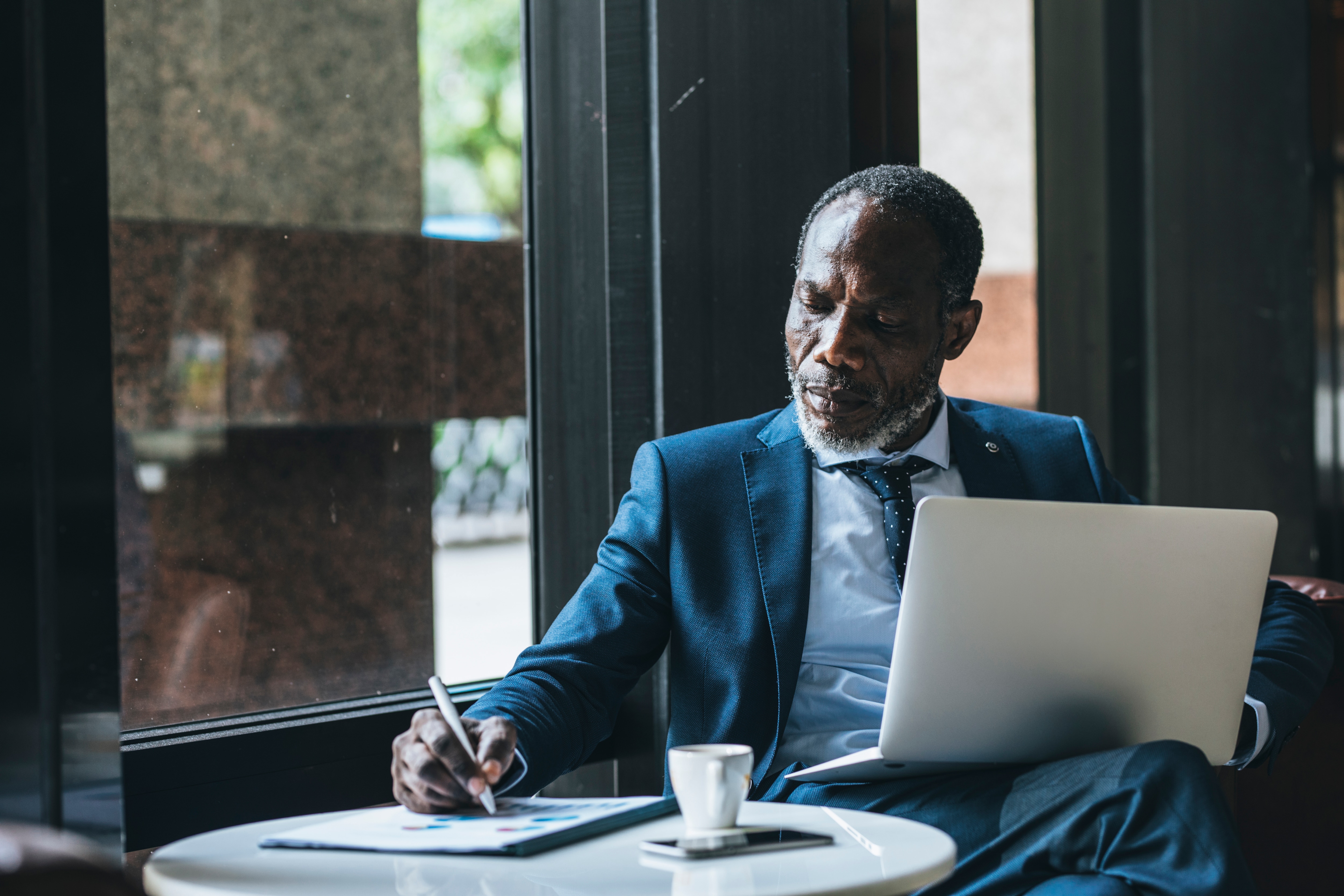 man reading physical document next to a laptop